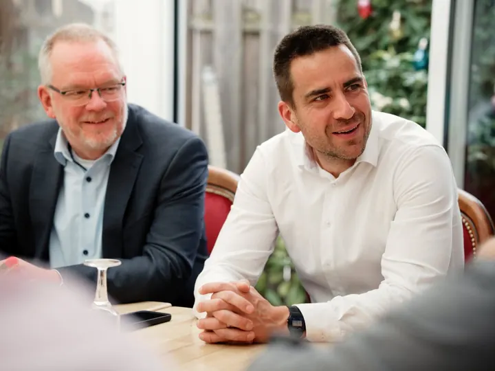 Daniel Phiesel und ein Mann hören bei einem Gespräch am Tisch zu.