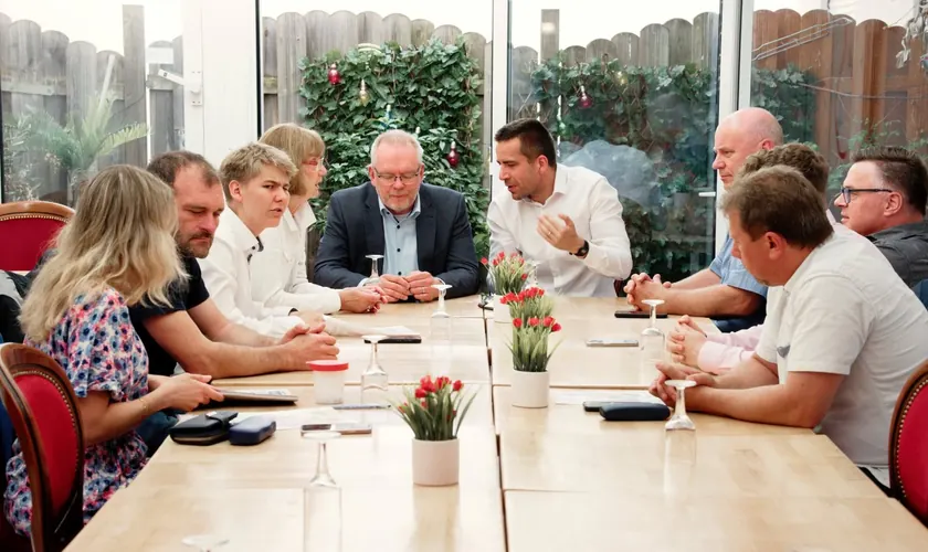 Mehrere Menschen sitzen an einem langen Tisch und unterhalten sich.