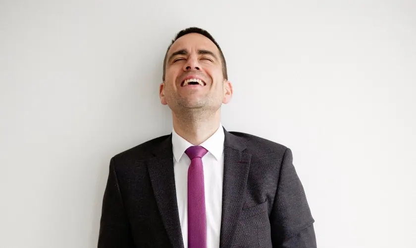 Daniel Phiesel lacht, im dunklen Anzug mit violetter Krawatte.